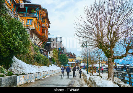 HALLSTATT, AUSTRIA - FEBRUARY 21, 2019: Walk the quiet winter lakeside promenade - Seestrasse with snowdrifts on the sides and colorful wooden houses  Stock Photo