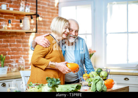 Cheerful senior couple cooking food with healthy fresh ingredients on the kitchen at home. Concept of healthy nutrition in older age Stock Photo