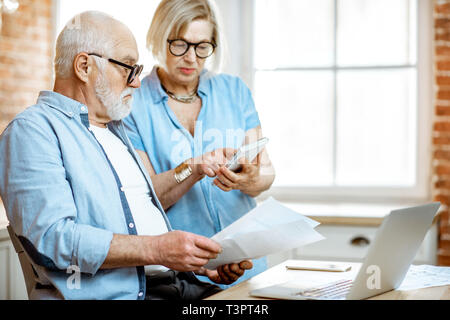 Senior couple with embarrassed emotions calculating some bills or taxes sitting with laptop on the kitchen at home Stock Photo