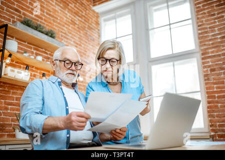 Senior couple with embarrassed emotions calculating some bills or taxes sitting with laptop on the kitchen at home Stock Photo