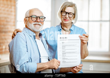 Portrait of a happy senior couple holding resume document indoors. Concept of work in older age Stock Photo