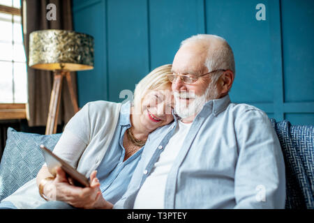 Lovely senior couple dressed casually using digital tablet while sitting together on the comfortable couch at home Stock Photo