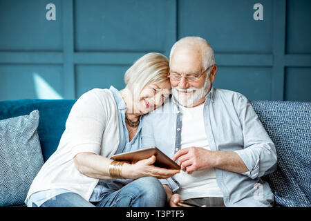 Lovely senior couple dressed casually using digital tablet while sitting together on the comfortable couch at home Stock Photo