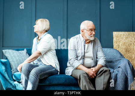 Offended senior man and woman feeling sad, sitting back to each other on the couch at home Stock Photo