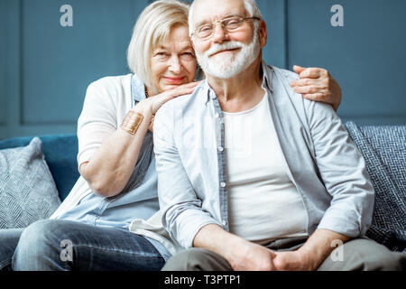 Portrait of a beautiful senior couple embracing each other, sitting on the couch at home Stock Photo