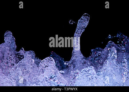 Blue-lit turbulent water forms futuristic shapes, shimmering with trapped air bubbles, rising against a black background like alien liquid sculpture. Stock Photo