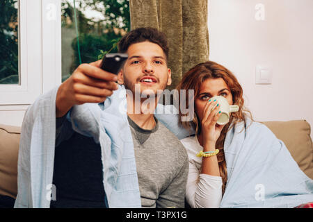 Young smiling heterosexual couple together on sofa using the remote control Stock Photo