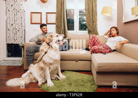 Young angry couple separated on sofa whit their dog using smartphone Stock Photo