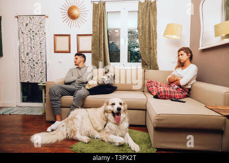 Young angry couple separated on sofa whit their dog using smartphone Stock Photo