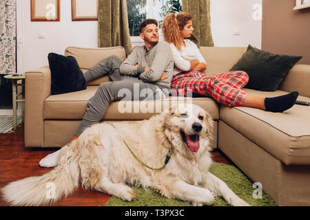 Young angry couple separated on sofa whit their dog using smartphone Stock Photo