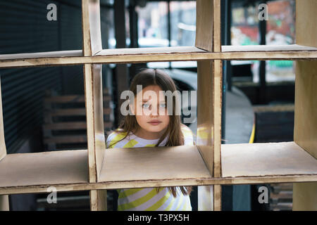 A pretty girl looking out from behind a cage-shaped structure. Play concept Stock Photo