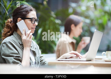Freelance manager talking on phone while using laptop Stock Photo