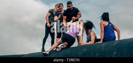 Group of participants in an obstacle course climbing a drum Stock Photo