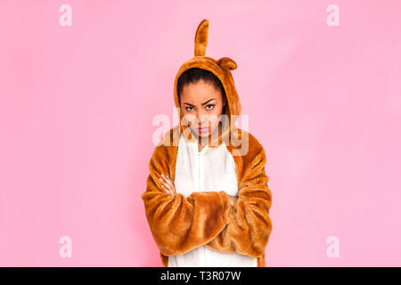 Young woman in bunny kigurumi standing isolated on pink background crossed arms looking camera angry Stock Photo