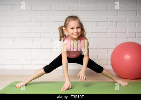 Cheerful little girl doing sports exercises on the mat at home, children's sports and yoga. Stock Photo