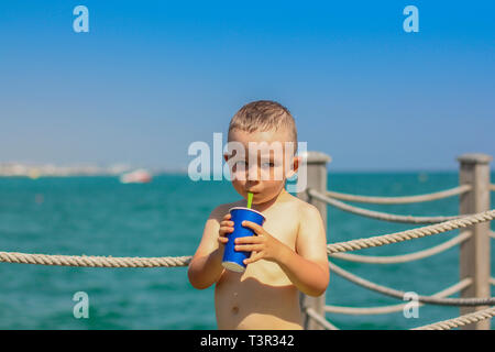 The boy drinks a drink from a paper cup through a straw. Summer holiday at the sea in Turkey, Antalya Stock Photo