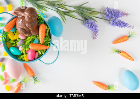 Easter basket with mini carrots, chocolate bunny, flowers, and Easter eggs on white background Stock Photo