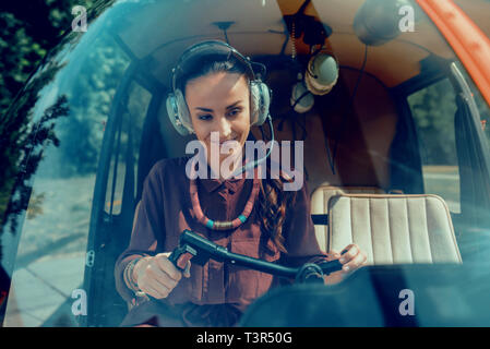 Joyful appealing woman wearing special headphones while being helicopter pilot Stock Photo