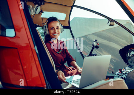 Cheerful dark-haired woman with wide smile placing silver laptop on front seat Stock Photo