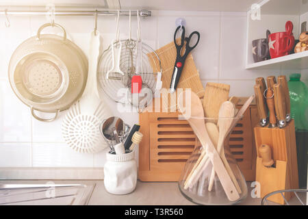 kitchen corner with various cooking utensils including a colander, knives and wooden utensils in a glass container Stock Photo