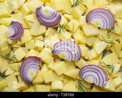 chopped raw potatoes in small pieces with red onion slices and rosemary leaves on top ready to be cooked in the oven Stock Photo