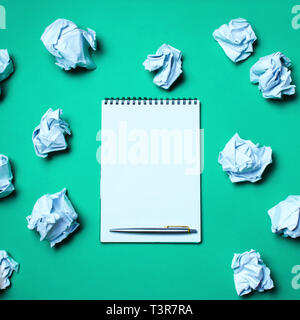 white notebook with pen on a green background among paper balls. The concept of generating ideas, inventing new ideas. Paper balls are all around. Sea Stock Photo