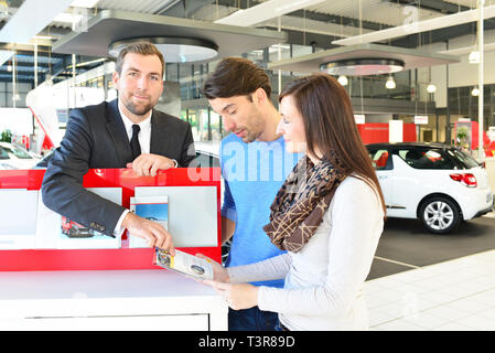 young couple buying a new car in the showroom of a car dealership with the seller Stock Photo
