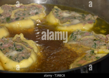 deliciois swabian maultaschen filled with spinach and meat, homemade rolled swabian meat ravioli floating in hot broth in a metal pot Stock Photo