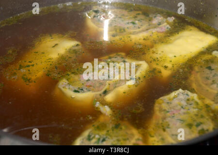 swabian ravioli  filled with spinach and meat in the soup as an appetizer, homemade rolled swabian meat ravioli floating in hot broth in a metal pot Stock Photo