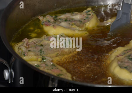homemade rolled swabian meat ravioli floating in hot broth in a metal pot, swabian maultaschen filled with spinach and meat Stock Photo