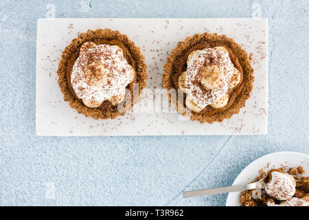 Closeup of homemade Banoffee Pie Tart with salted caramel, banana, whipping cream, decorated with grated chocolate. Top view. Stock Photo