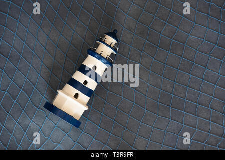 Little toy lighthouse on a dark background with a sea grid Stock Photo