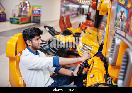 Asian guy compete on speed rider arcade game racing simulator machine. Stock Photo