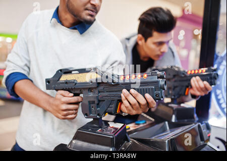 Two asian guys compete on shooter simulator game arcade machine. Stock Photo