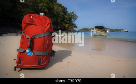 A red suitcase rests on a beach after being dropped off by a panga boat on Isla Coiba, Panama Stock Photo