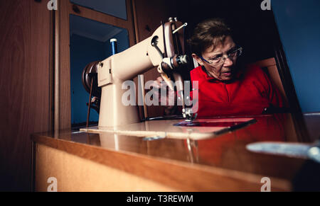 Indoor shot of beautiful elderly woman tailor sewing sock using stitching machine at her home, enjoying her hobby. People, occupation and job Stock Photo