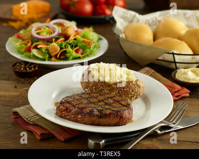 Sirloin steak with baked potato, salad, and dinner rolls Stock Photo