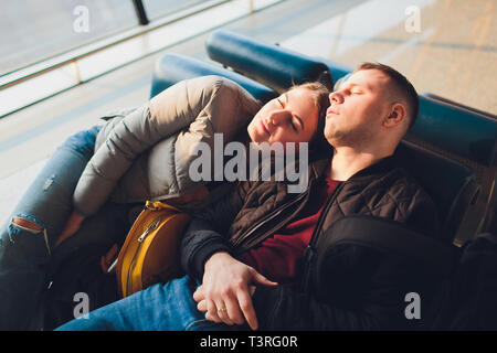 Young couple sleeping on the chairs at the waiting room of the airport. Long waiting for the airplane. Stock Photo