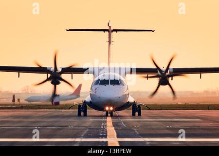 Front view of propeller airplane taxiing to runway for take off. Traffic at airpot at sunset. Stock Photo