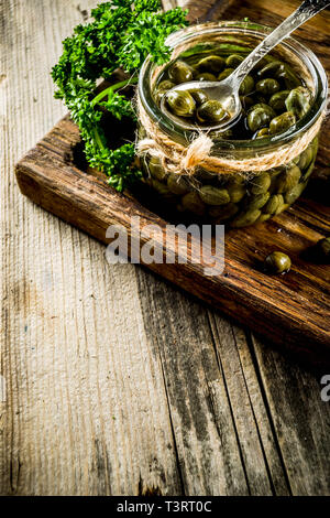 Pickled capers in little jar, with herbs on rustic wooden background copy space Stock Photo