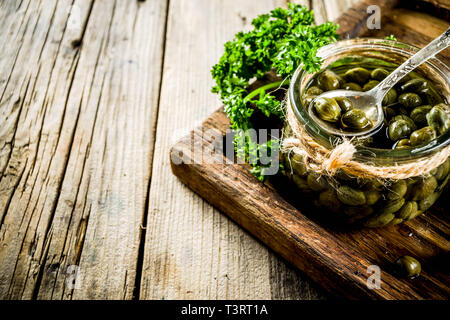 Pickled capers in little jar, with herbs on rustic wooden background copy space Stock Photo