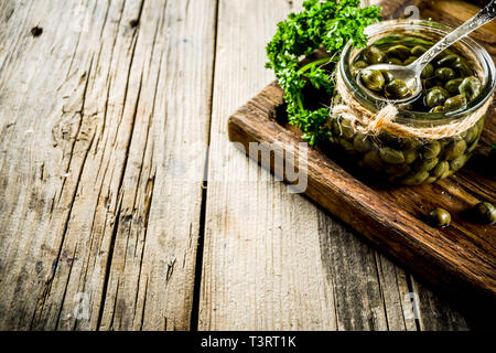 Pickled capers in little jar, with herbs on rustic wooden background copy space Stock Photo