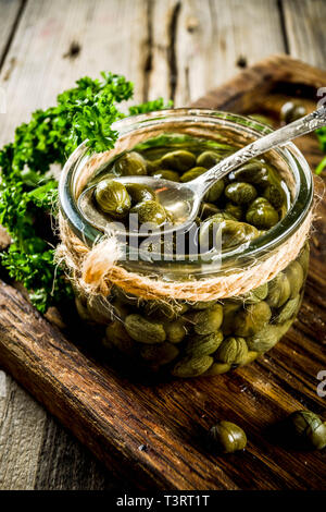 Pickled capers in little jar, with herbs on rustic wooden background copy space Stock Photo