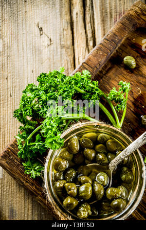 Pickled capers in little jar, with herbs on rustic wooden background copy space Stock Photo