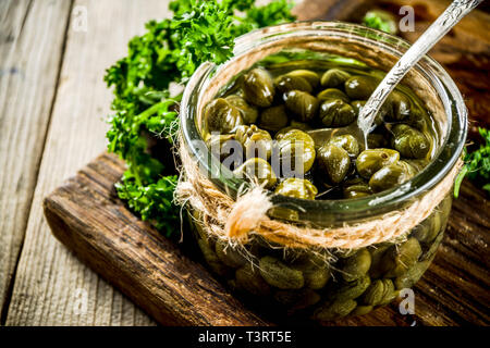 Pickled capers in little jar, with herbs on rustic wooden background copy space Stock Photo