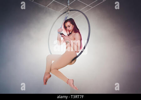 Aerial acrobat in the ring. A young girl performs the acrobatic elements in the air ring. uses the phone to prepare a photo shoot Stock Photo