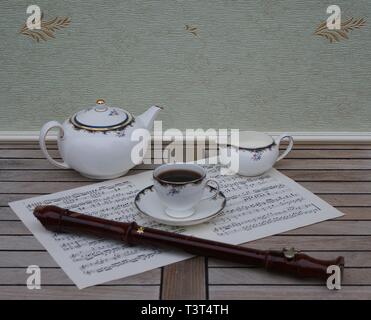 English teacup with saucer, teapot and cream jug, fine bone china porcelain, and a block flute on a sheet of music Stock Photo