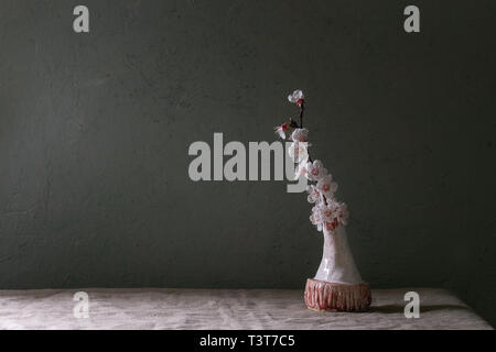 Spring blossom cherry branch flowers in craft ceramic vase standing on grey linen table cloth. Spring interior. Copy space. Stock Photo