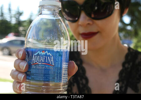 Beautiful dark haired girl on a bright sunny day in the park having a drink of purified water. Stock Photo