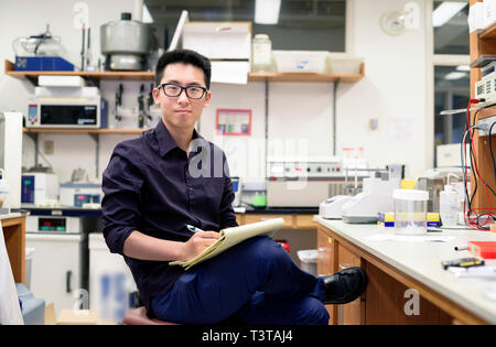 Asian man writing on notepad in electronics workshop Stock Photo